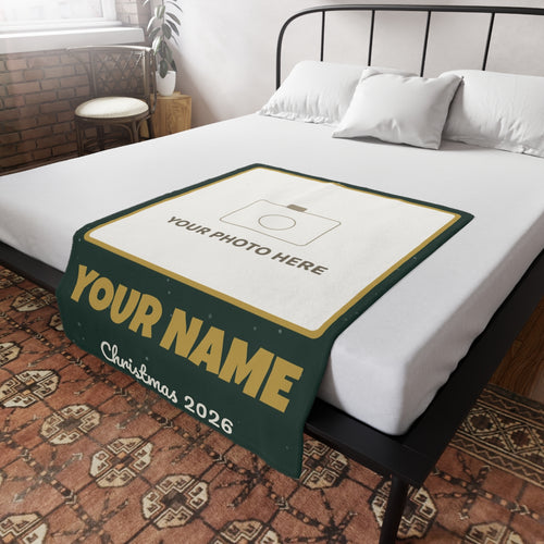 Personalised photo blanket laid on a bed, with a photo panel, a name and Christmas 2026 on a green and gold border